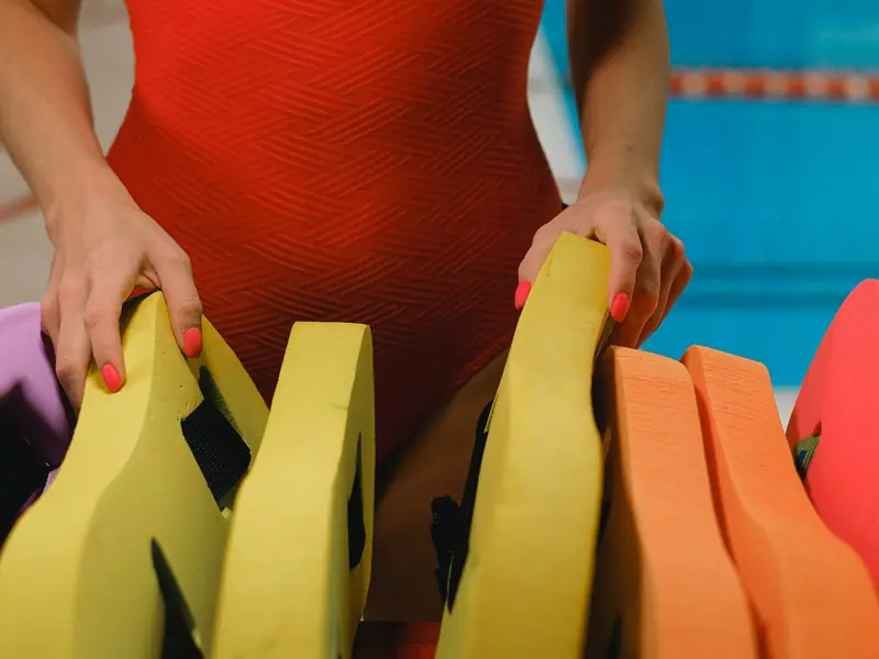 A swim teacher in a red swimsuit setting out kickboards by the pool