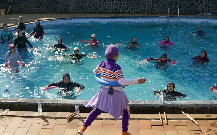 A teacher on the pool deck leading a water class full of swimmers