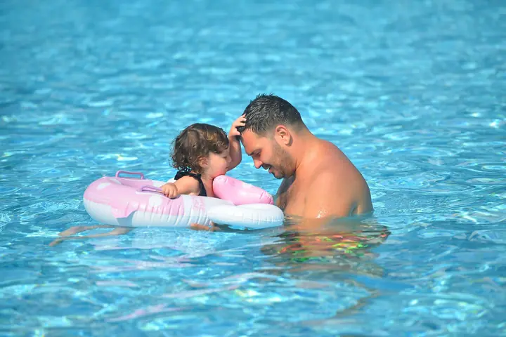 A father and his toddler, forehead to forehead, in an outdoor pool