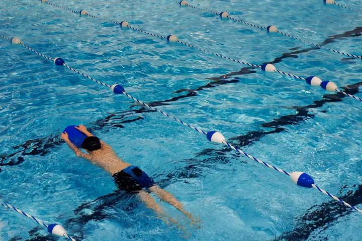A swimmer from behind, kicking down a lane with a kickboard