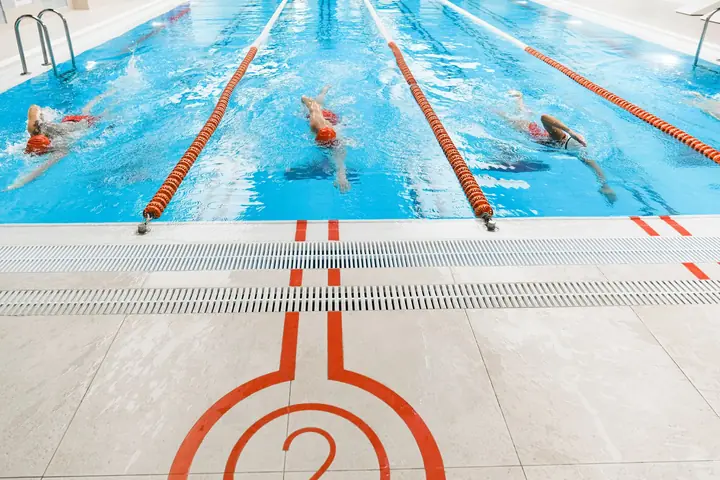 Three swimmers training side by side in an indoor lane pool