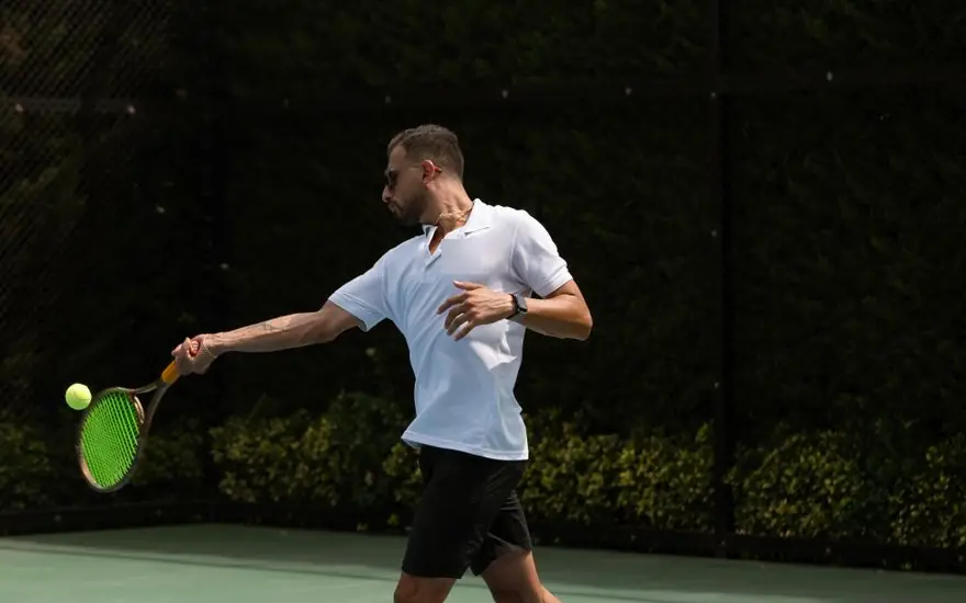A tennis coach hitting a forehand on an outdoor hard court
