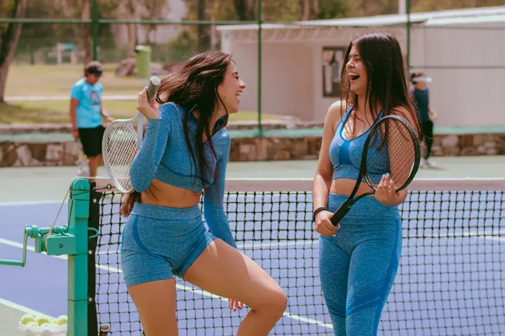 Two women laughing by the net with their rackets