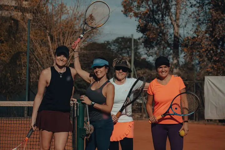 Four women with rackets smiling together on a clay court