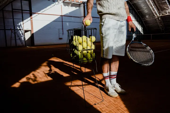 A coach by a basket of balls, picking one out to feed